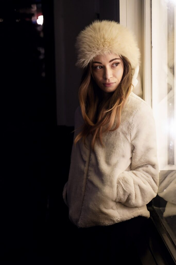 Liz leaning against an illuminated window, softly lit by its glow during a night photoshoot in Mayfair, London.